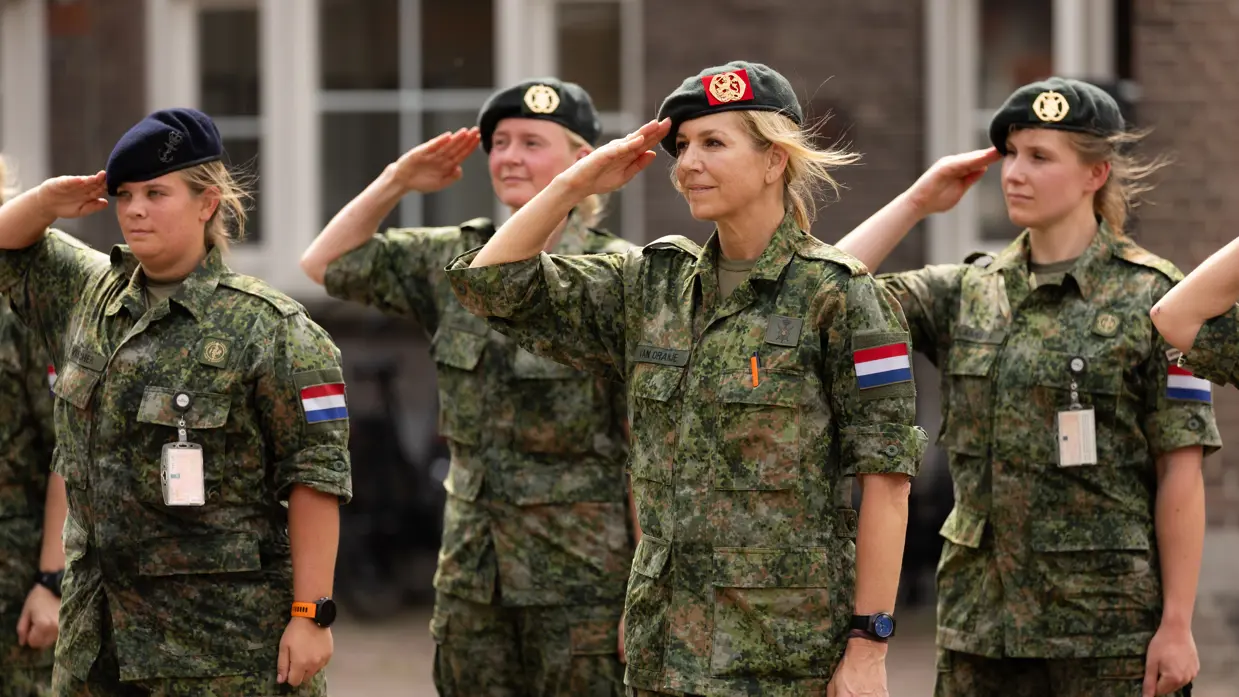 Koningin Máxima brengt met haar baret op de militaire groet tussen drie andere militairen. 