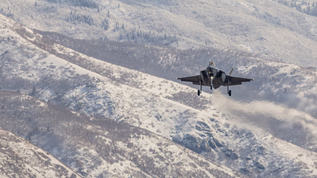 Een F-35 vliegend boven besneeuwd berglandschap.