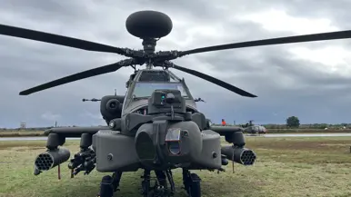 Een grote zwarte militaire helikopter staat op een betonnen baan met een grijze lucht er boven. 