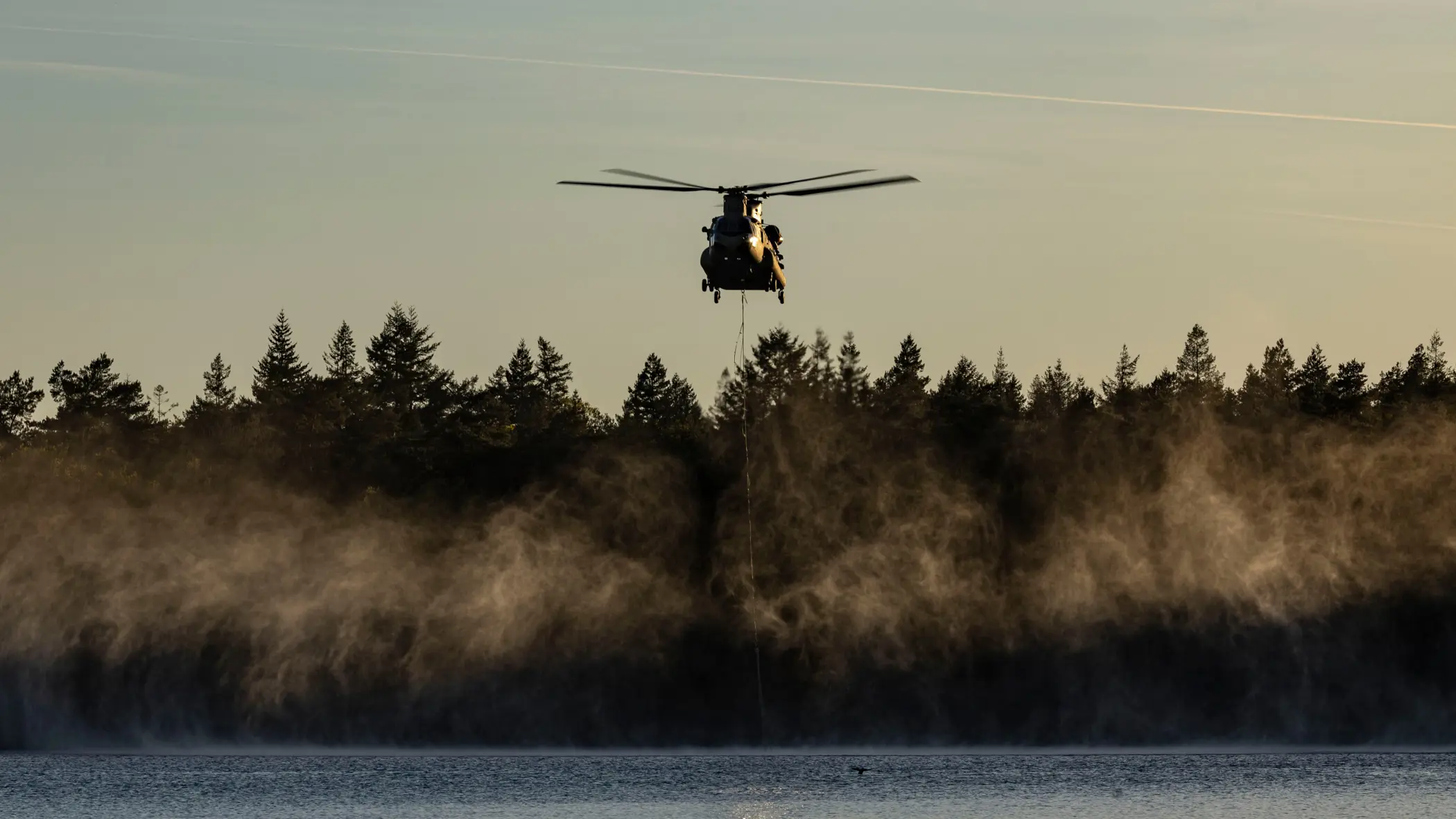 Een helikopter met waterzak boven het water.