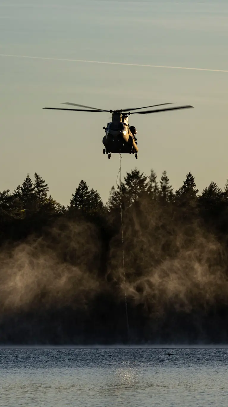 Een helikopter met waterzak boven het water.
