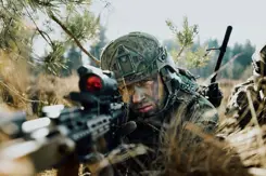 Een militair in de bosjes kijkt door een wapen.