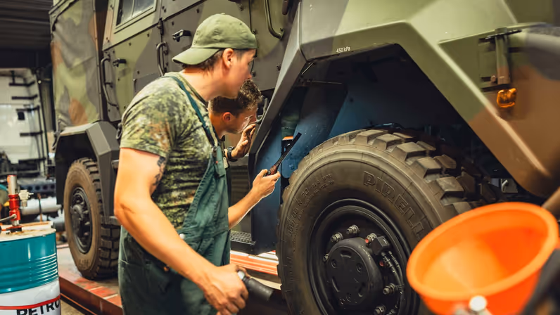 Twee militairen in groene overall kijken met een lampje in de wielkast van de militaire Manticore.