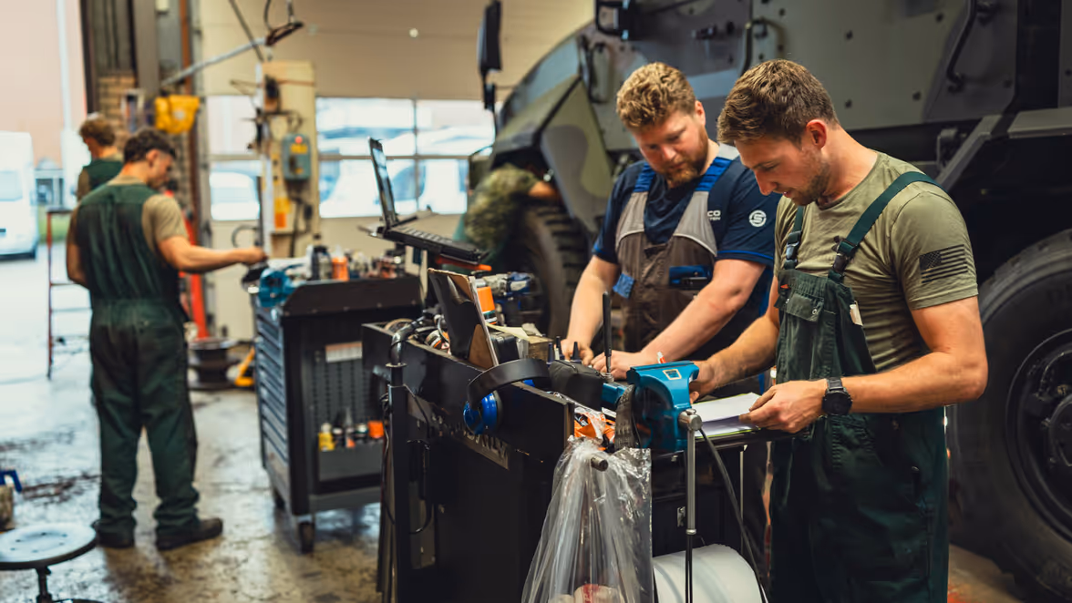 Een burgermedewerker van Iveco en een militair kijken naar een computerscherm. Achter hen is de Manticore op de werkplaats te zien.