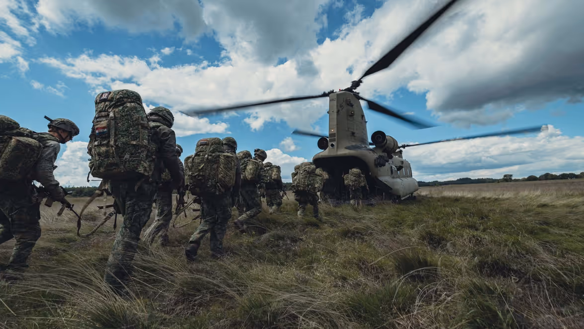 Militairen lopen achter elkaar aan over de heide naar de achterklep van de Chinook en stappen in de helikopter.