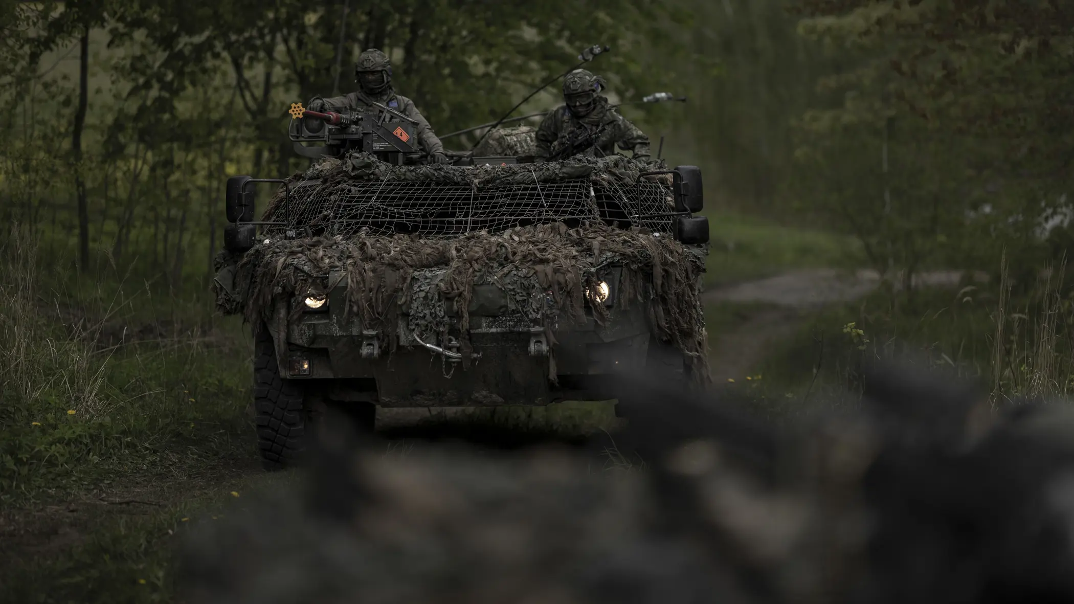Een Fennek-verkenningsvoertuig met twee militairen rijdt door een beboste omgeving.