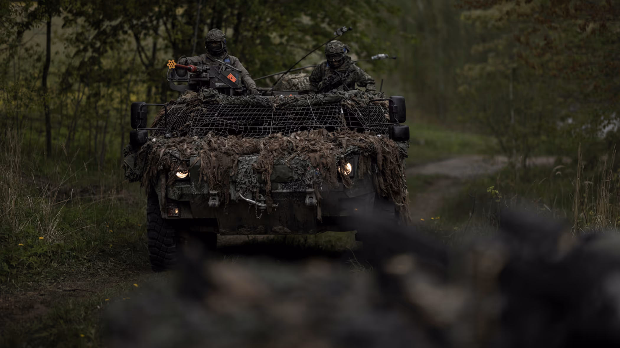 Een Fennek-verkenningsvoertuig met twee militairen rijdt door een beboste omgeving.
