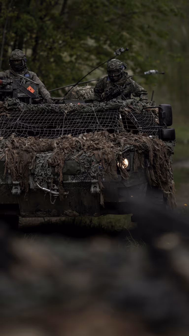 Een Fennek-verkenningsvoertuig met twee militairen rijdt door een beboste omgeving.