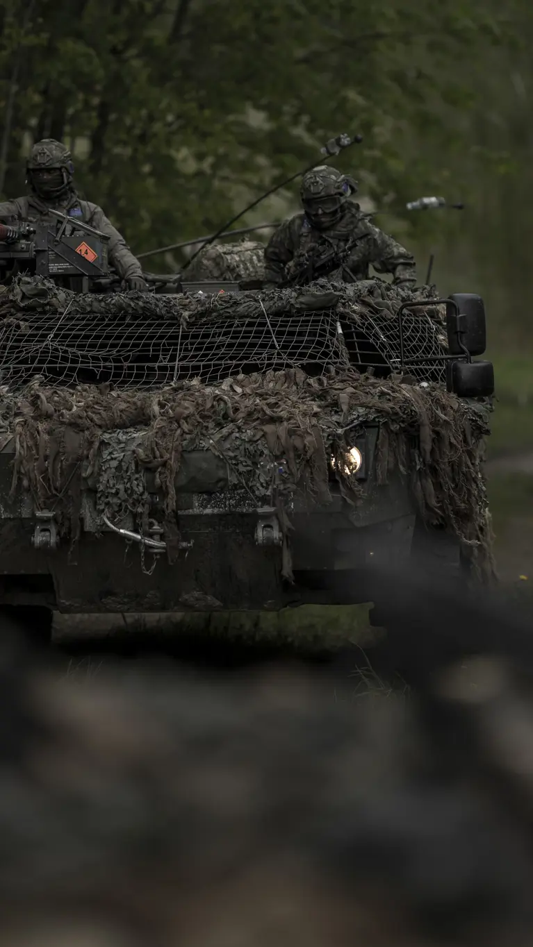 Een Fennek-verkenningsvoertuig met twee militairen rijdt door een beboste omgeving.