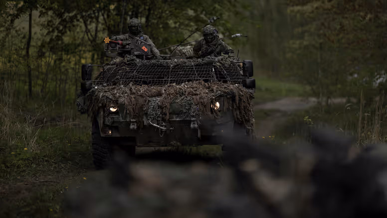 Een Fennek-verkenningsvoertuig met twee militairen rijdt door een beboste omgeving.