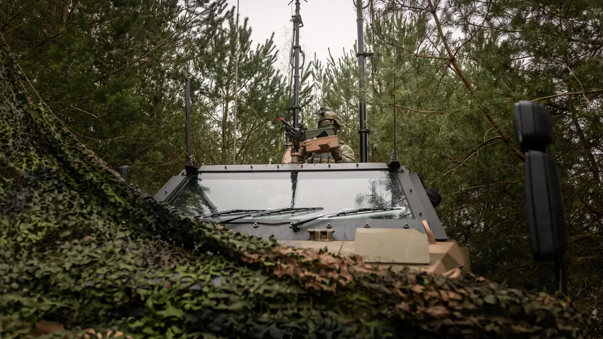 Een Bushmaster in het zijterrein. Boven het gepantserde voertuig torenen diverse antennes. 