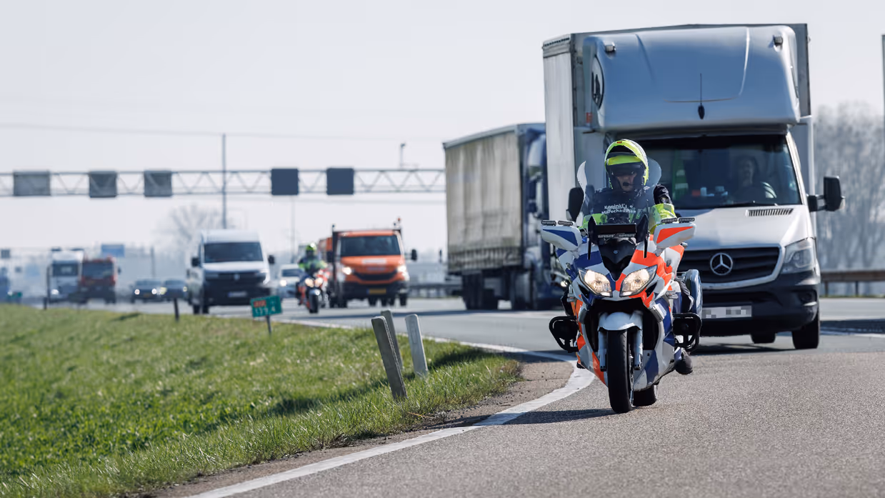 Een motor van de Koninklijke Marechaussee met daarachter een rits voertuigen.