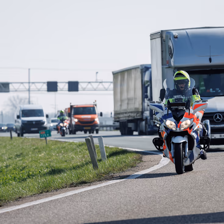 Een motor van de Koninklijke Marechaussee met daarachter een rits voertuigen.