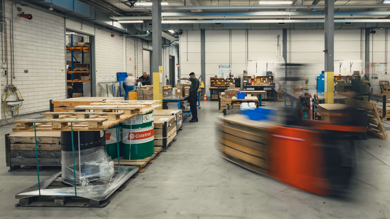 Het grijze depot van het DBBB. Hierop zijn onder meer medewerkers, pallets, vaten olie en een langsrijdende heftruck te zien.&nbsp;