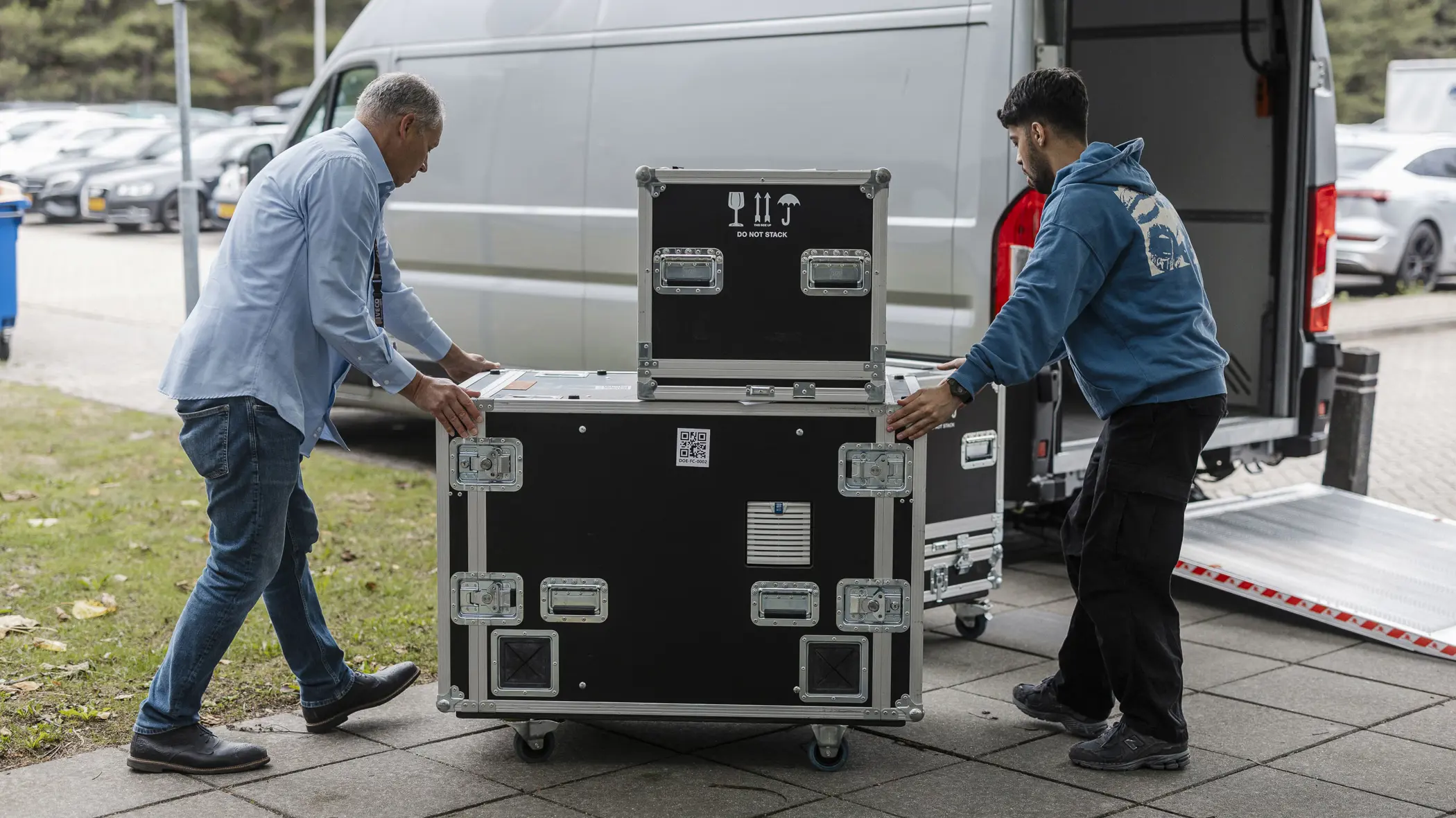 Twee medewerkers rollen flightcases met ICT-apparatuur uit een bestelbus tijdens de opbouw voor Falcon Leap.