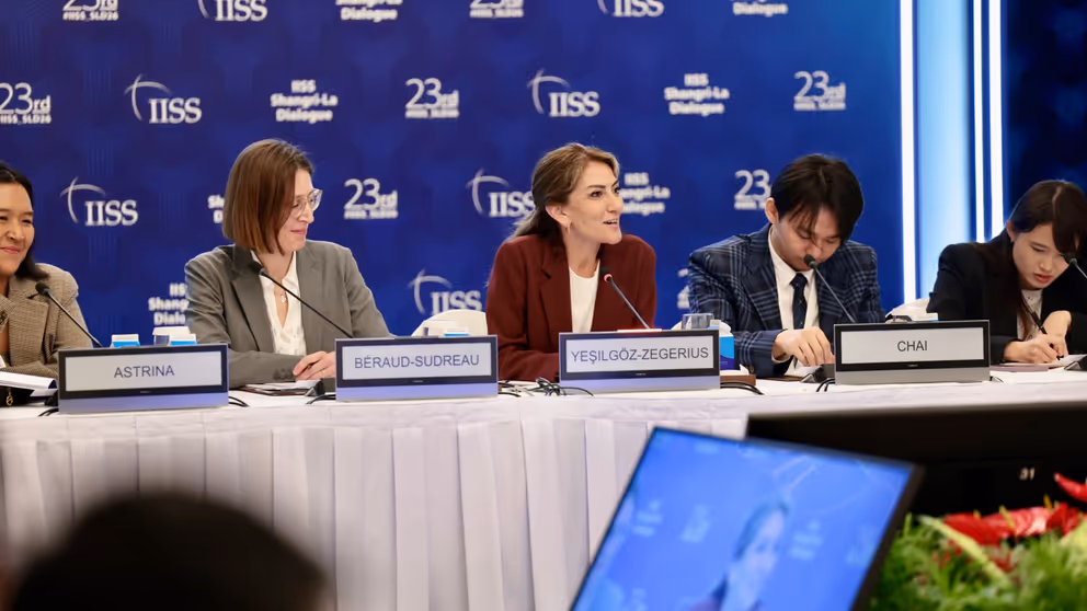 De minister zit achter een tafel met haar internationale collega's.