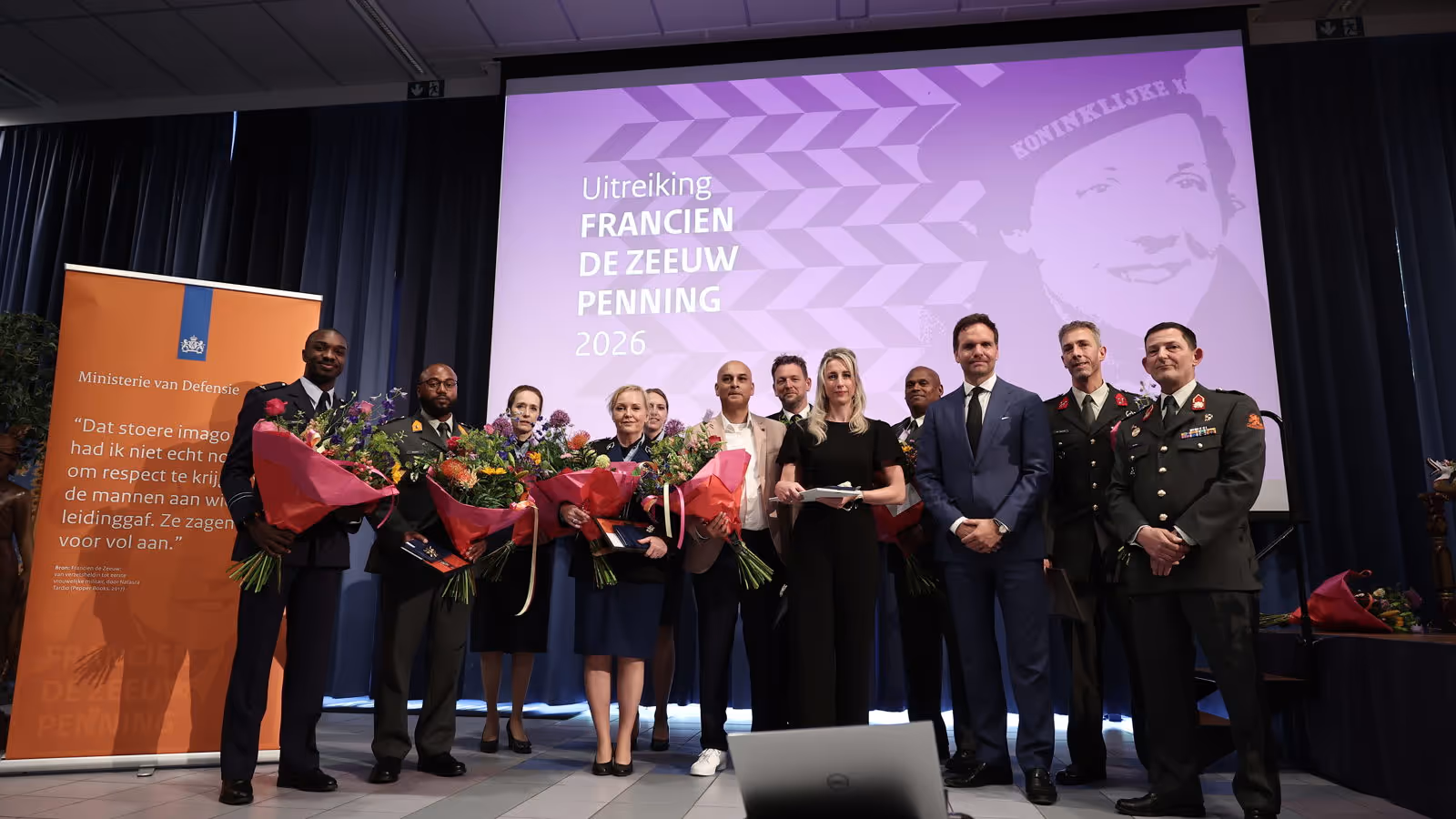 Twaalf personen, van wie het merendeel in militair uniform, poseren naast elkaar met ieder een bos bloemen in de hand.
