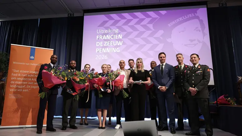 Twaalf personen, van wie het merendeel in militair uniform, poseren naast elkaar met ieder een bos bloemen in de hand.