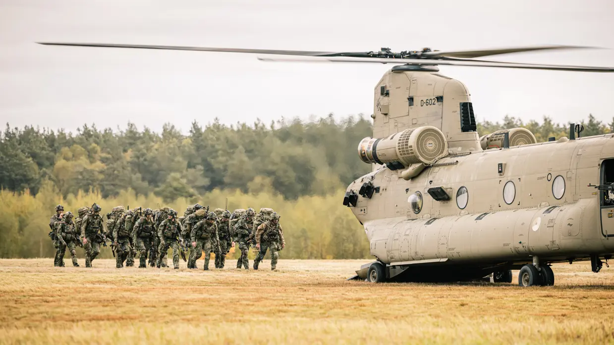 Bepakte infanteristen lopen in een veld naar een Chinook