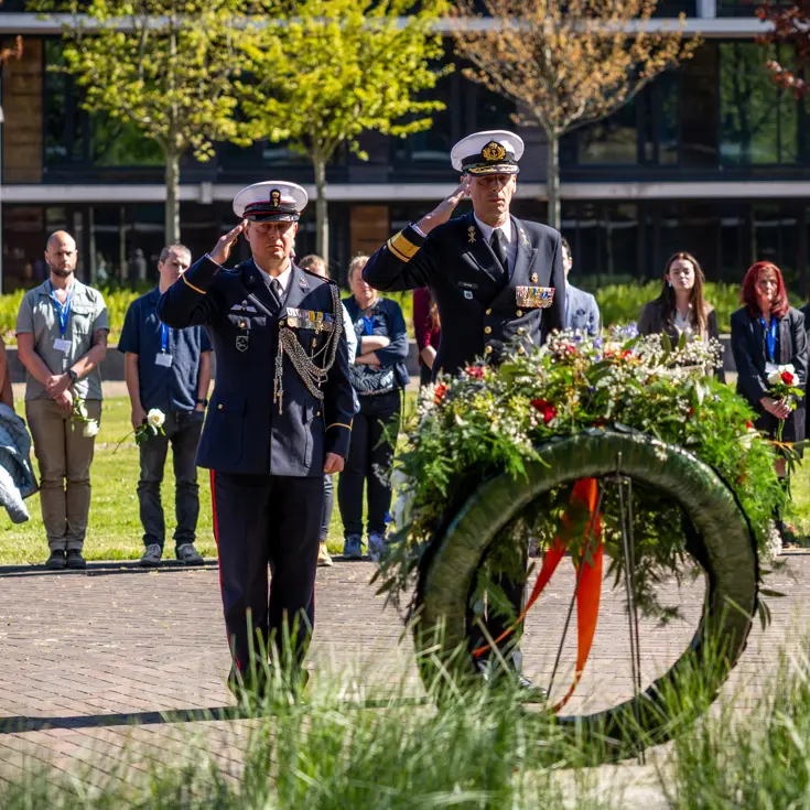 Vice-admiraal Jan Willem Hartman en adjudant Johan Nagel salueren naar de zojuist gelegde krans. Achter hen staan de nabestaanden. 
