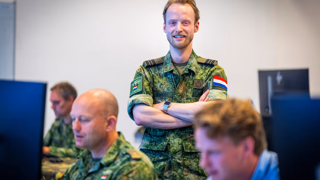 Een militair van de luchtmacht poseert met voor hem twee militairen en een burgermedewerker.