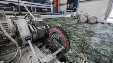 Stof met groen camouflagepatroon wordt door machine geleid tijdens controle op productiefouten.