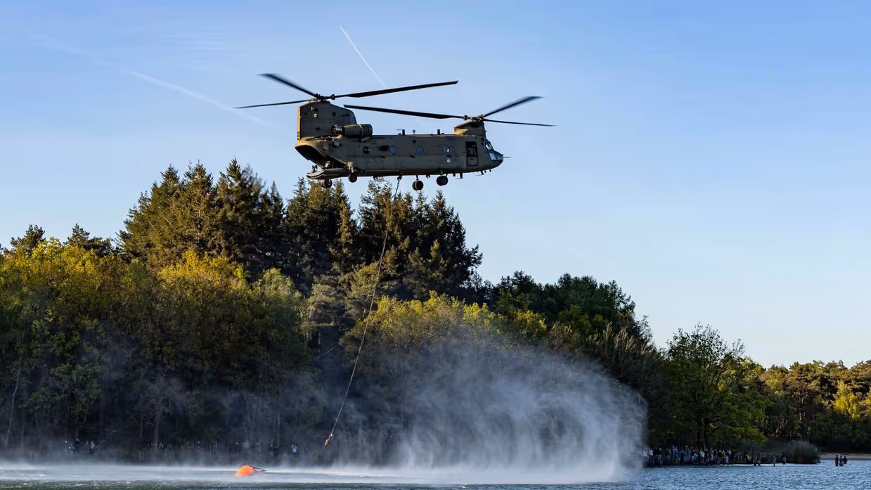 Een helikopter vult de waterzak die eronder hangt. 