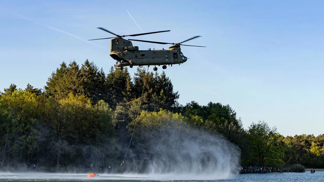 Een helikopter vult de waterzak die eronder hangt. 