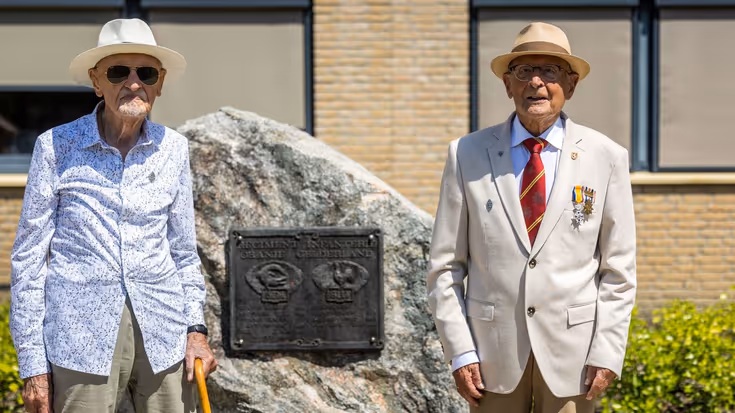 Twee veteranen poseren naast een monument.