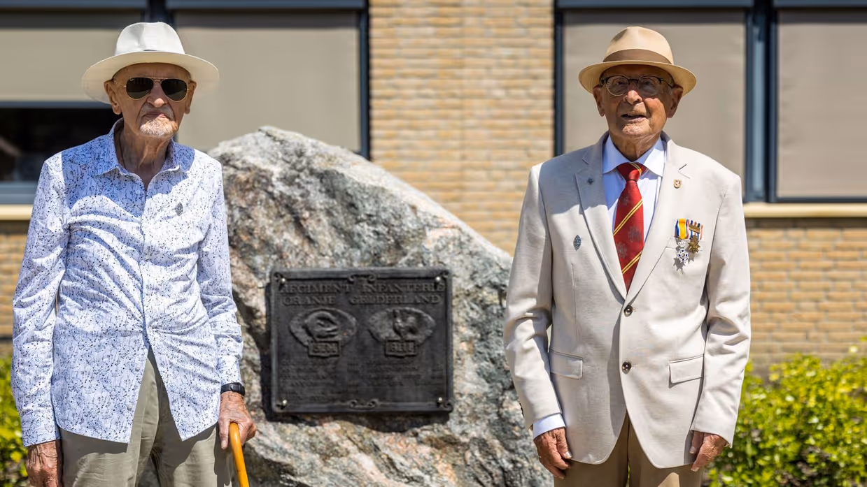 2 veteranen poseren naast een gedenksteen.&nbsp;