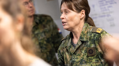 Links: Drie militairen in uniform staan in gesprek. Een man wijst uitleggend naar voren, een vrouw luistert aandachtig, en een andere man staat met gekruiste armen. Rechts: Een vrouw in militair uniform met naam praat serieus tijdens een bespreking. Op de achtergrond staan collega's in uniform bij een whiteboard. 