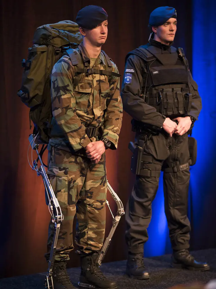 Twee mannen in uniform: één met camouflage, rugzak en exoskelet, de andere in zwart met kogelwerend vest.