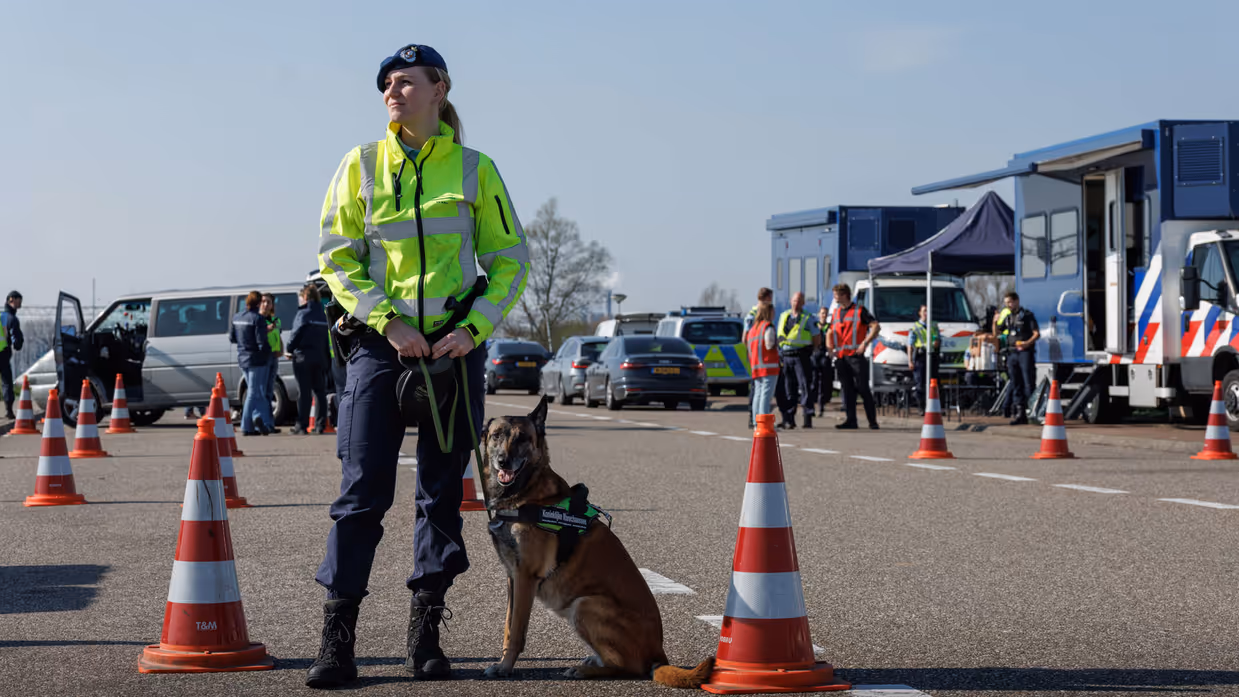Een vrouwelijke marechaussee met een hond aan haar zijde.