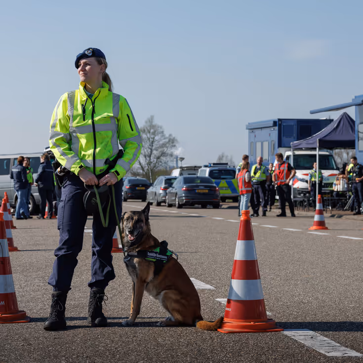 Een vrouwelijke marechaussee met een hond aan haar zijde.