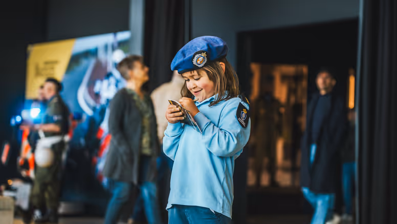 Klein meisje in Marechaussee-uniform met een boekje in haar hand.