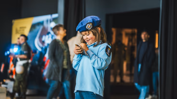 Klein meisje in Marechaussee-uniform met een boekje in haar hand.