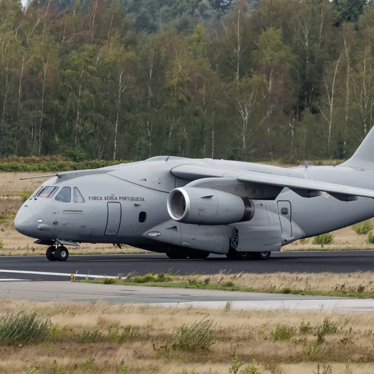  Een grijs militair transportvliegtuig van de Portugese luchtmacht rollend op een startbaan met gras, bomen en een bewolkte lucht. 