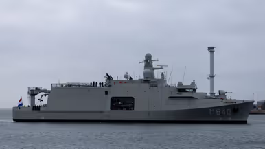 Het varende, grijze marineschip vanaf de zijkant. Daarnaast een afbeelding met daarop een deel van de bemanning bij de reling van het schip, daarachter een wapperende Nederlandse vlag. Vervolgens saluerende militairen vanaf de brug van de Vlissingen en een groepje marineofficieren dat het schip vanaf de kade aanschouwt en vastlegt met de mobiele telefoon.