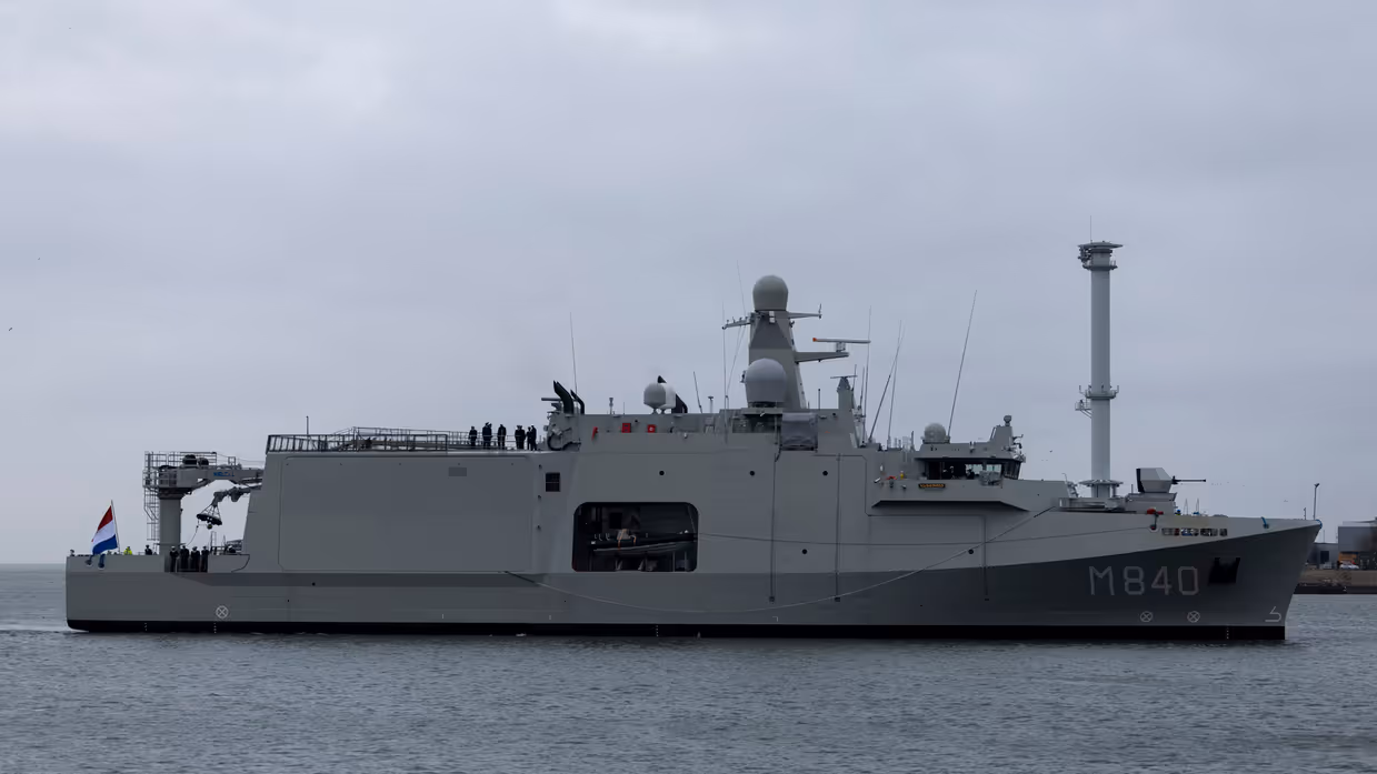 Het varende, grijze marineschip vanaf de zijkant. Daarnaast een afbeelding met daarop een deel van de bemanning bij de reling van het schip, daarachter een wapperende Nederlandse vlag. Vervolgens saluerende militairen vanaf de brug van de Vlissingen en een groepje marineofficieren dat het schip vanaf de kade aanschouwt en vastlegt met de mobiele telefoon.