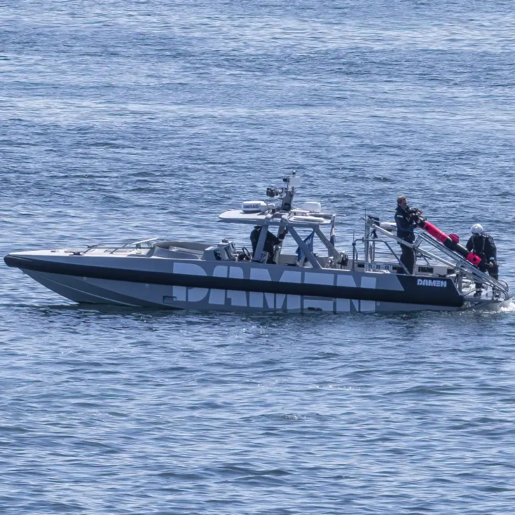 Een kleine boot ligt stil op het water; aan de achterkant hangt een ronde onderwaterdrone.