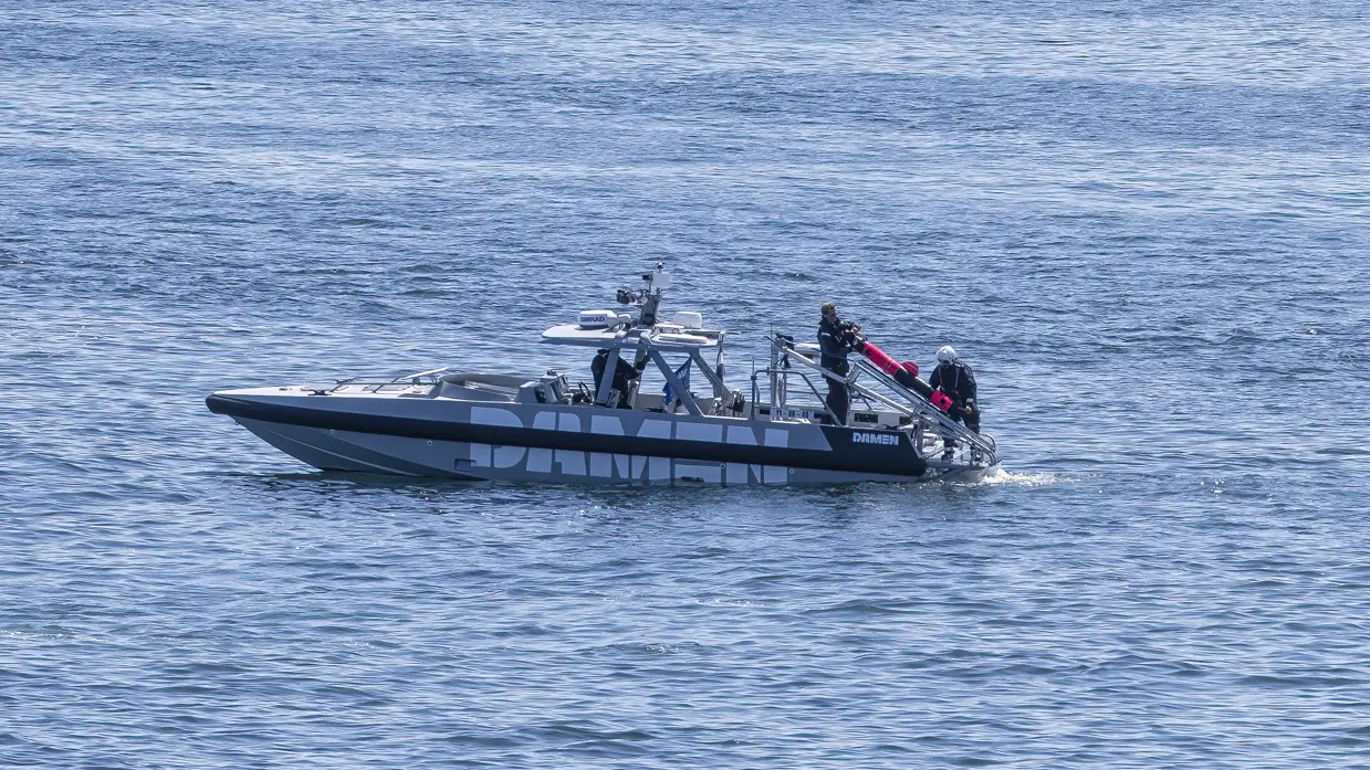 Een kleine boot ligt stil op het water; aan de achterkant hangt een ronde onderwaterdrone.