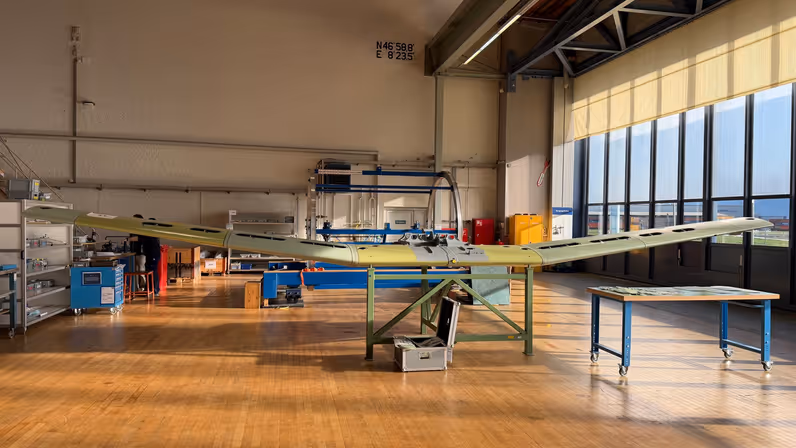 Een vliegtuigvleugel ligt op werkbank in een hal. 