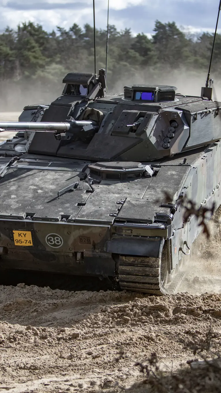 Een CV90 rijdt door een zanderig oefenterrein. 