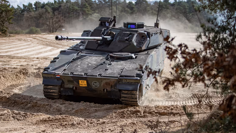 Een CV90 rijdt door een zanderig oefenterrein. 