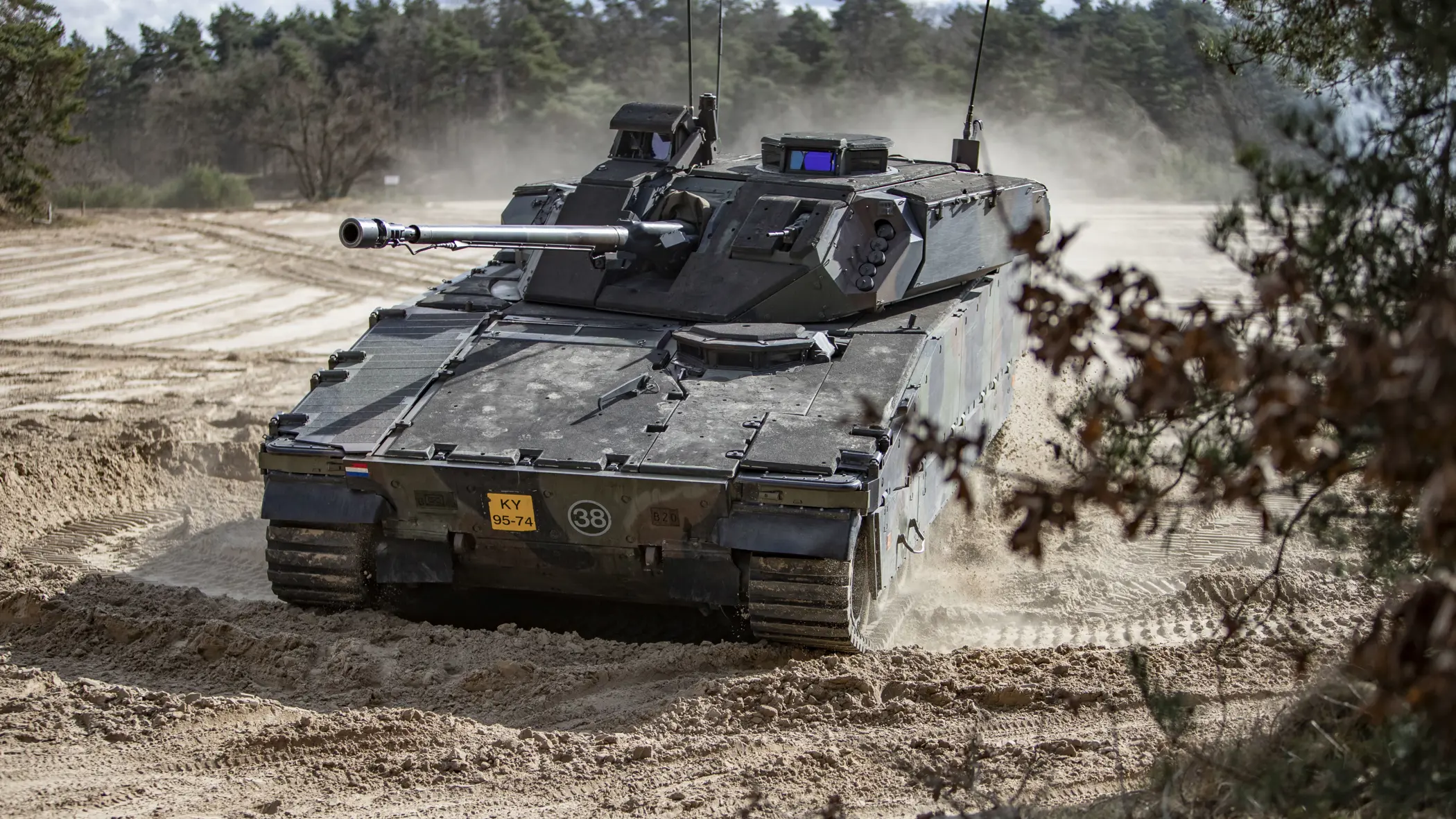 Een CV90 rijdt door een zanderig oefenterrein. 