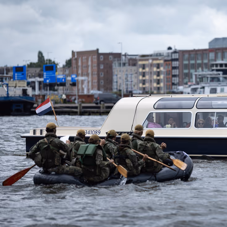 De deelnemers aan de NWT roeien in rubberboten door Amsterdam.