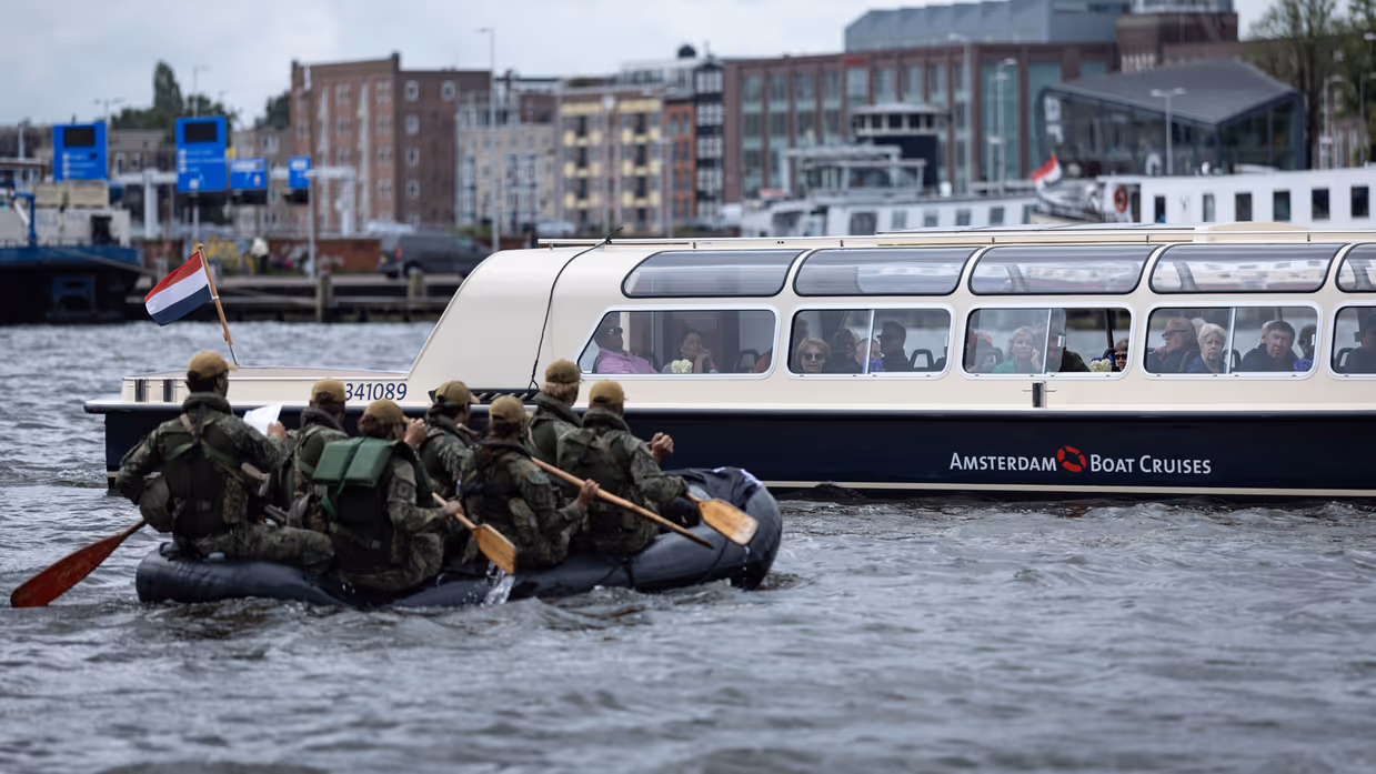 De deelnemers aan de NWT roeien in rubberboten door Amsterdam.