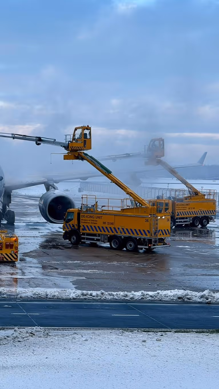 Een vliegtuig op een besneeuwde luchthaven, waar gele de-icing voertuigen met lange armen ijs van de vleugels verwijderen voor een veilige vlucht.