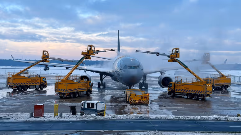 Een vliegtuig op een besneeuwde luchthaven, waar gele de-icing voertuigen met lange armen ijs van de vleugels verwijderen voor een veilige vlucht.