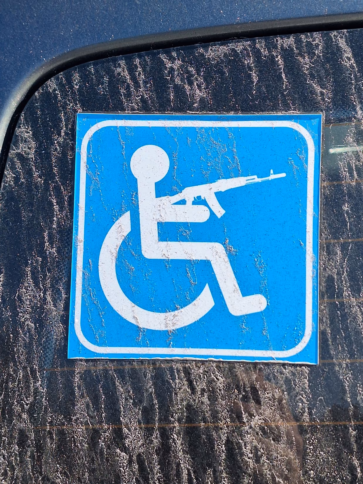 Een groot, liggend stenen beeld van een persoon, half ingebed in een betonnen blok, naast een modern gebouw met geparkeerde auto’s en een heldere lucht.